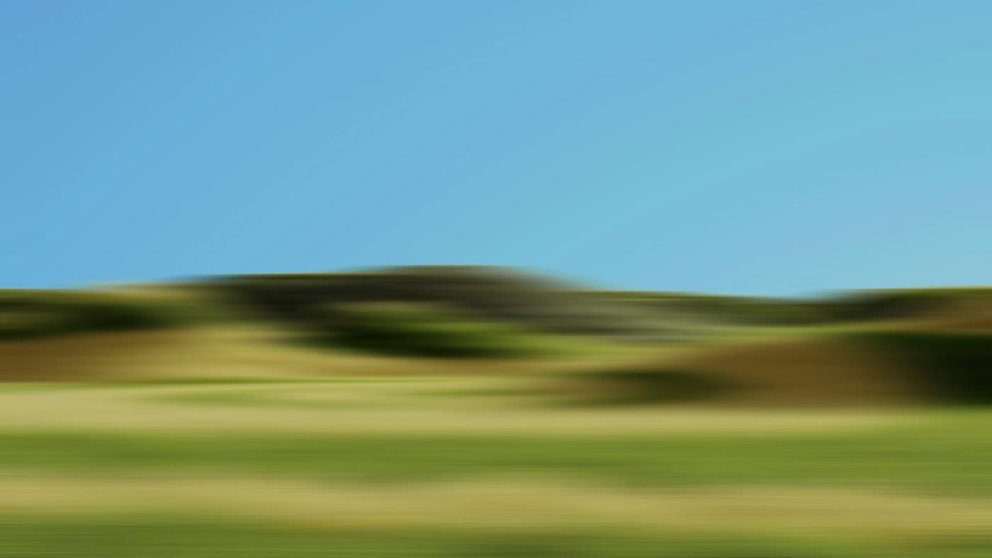Green hills under a blue sky, blurred by motion