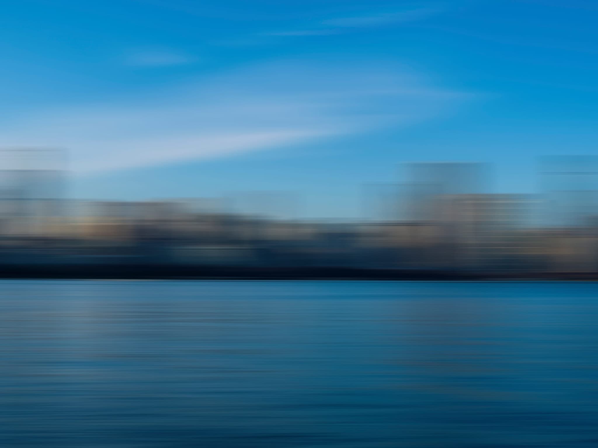 City skyline across blue water, blurred by motion