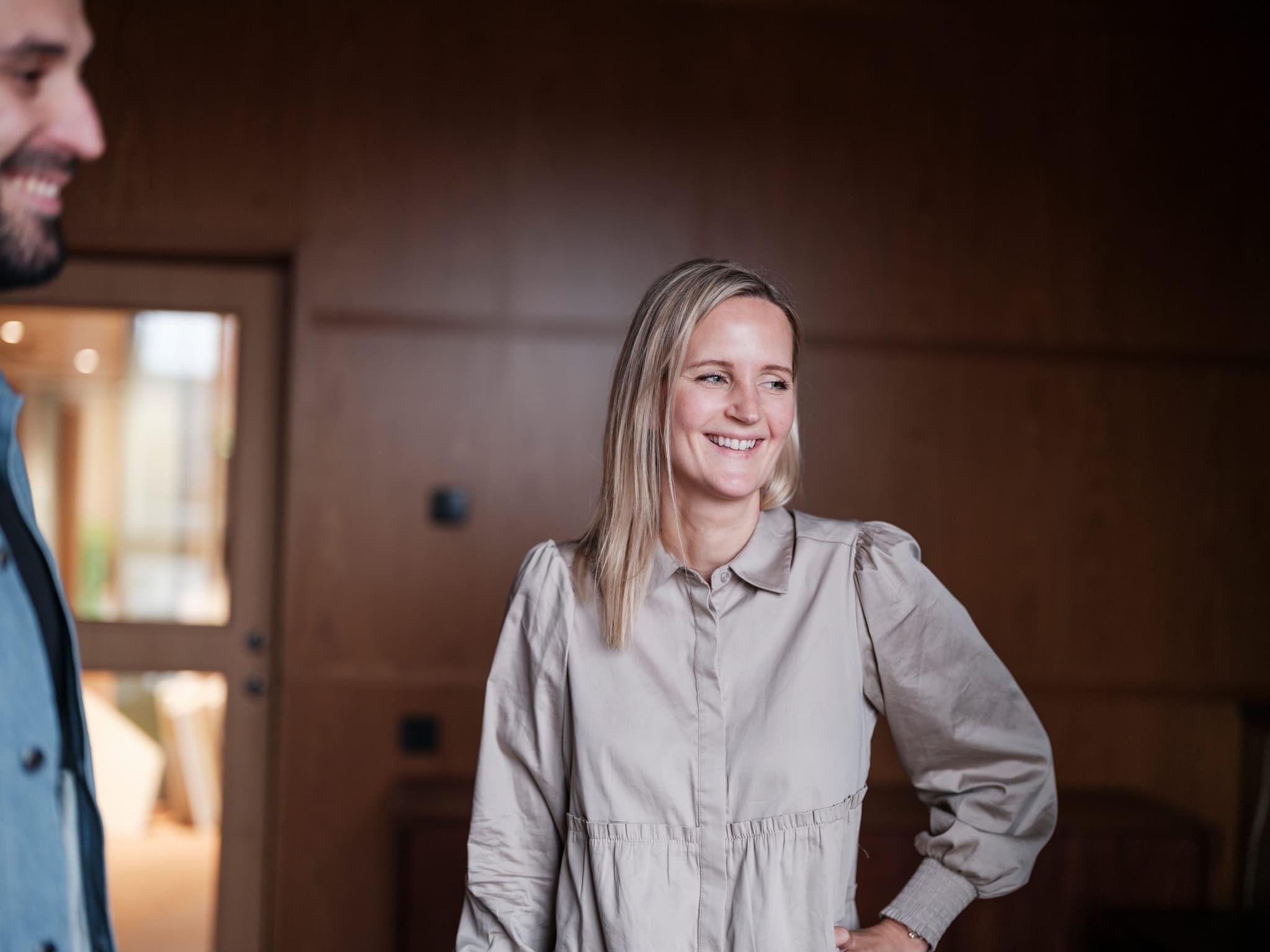 A Curamando consultant standing in a wood-panelled meeting room, smiling at a colleague